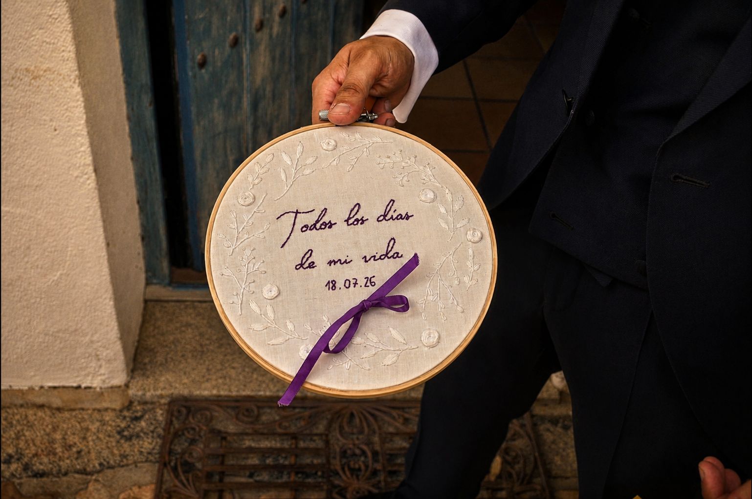 El novio sostiene un bastidor bordado a mano que dice «Todos los días de mi vida» con la fecha de la boda