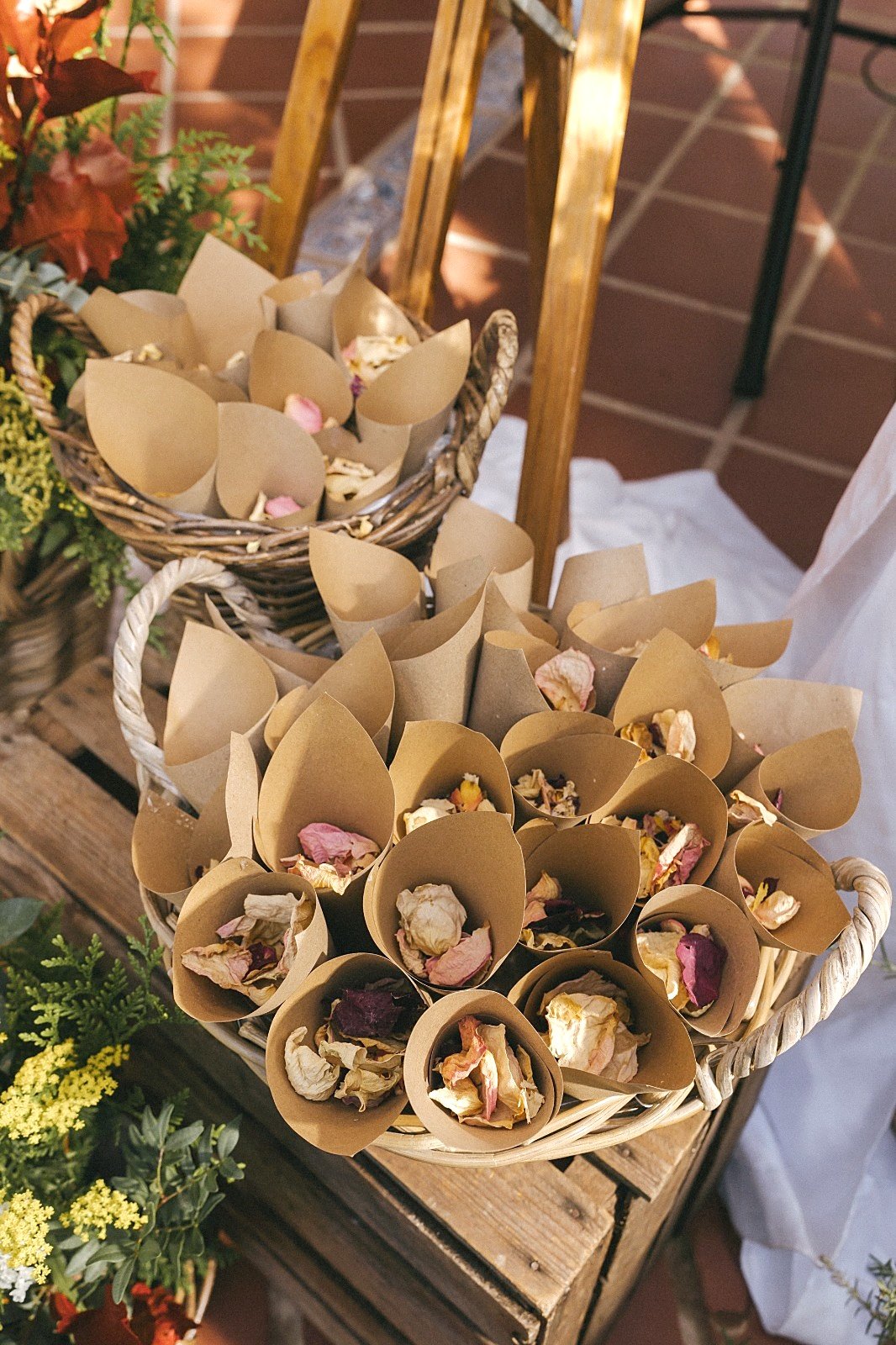 Cestas de mimbre con conos de papel kraft llenos de pétalos secos para recibir a los novios