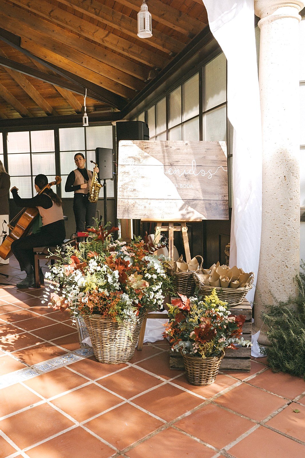 Dos músicas tocan el chelo y el saxofón junto al cartel de bienvenida y cestas de flores de otoño