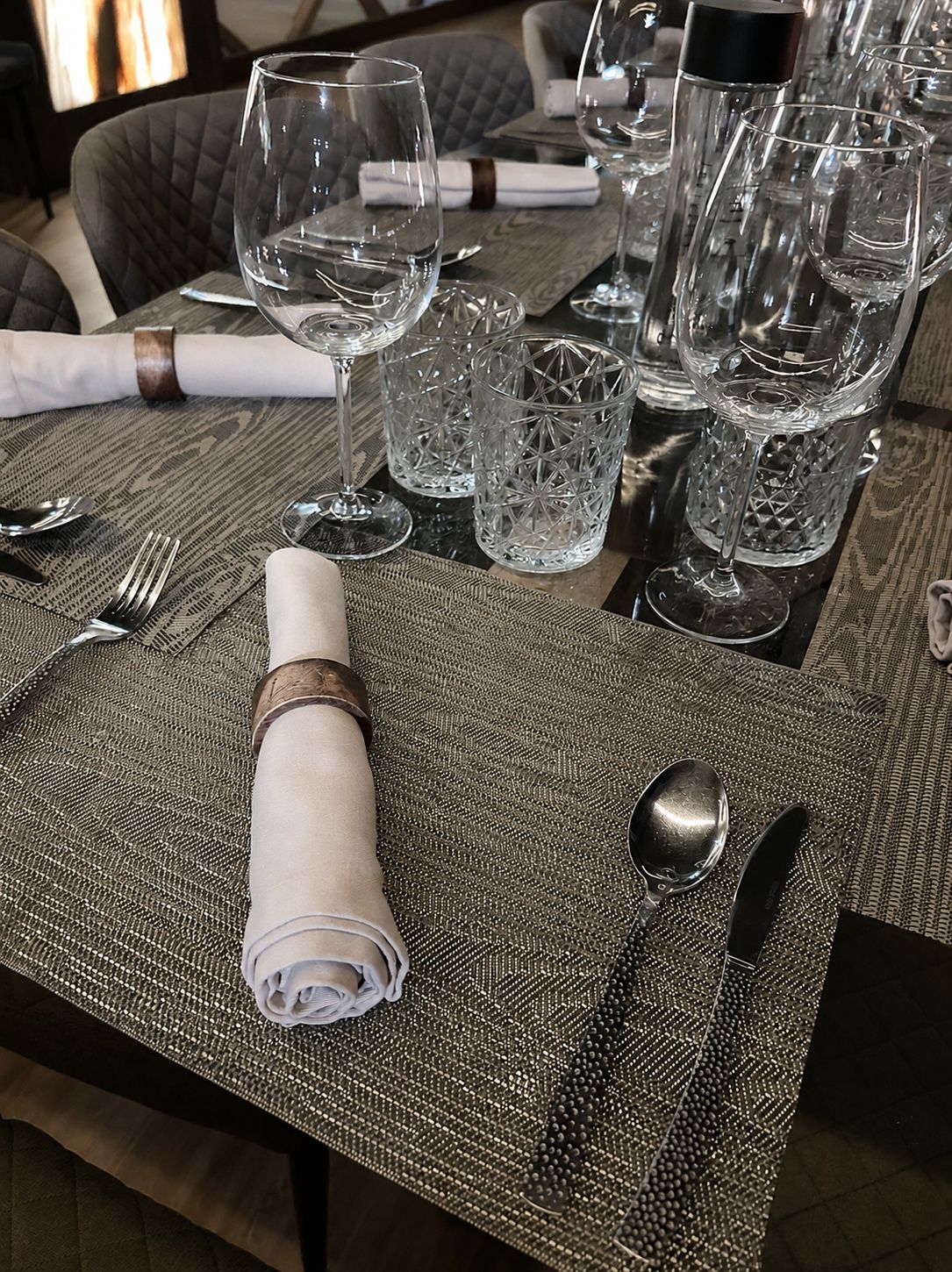 Detalle de un cubierto de la mesa: servilleta enrollada con anilla de madera, cristalería tallada y mantel individual tejido