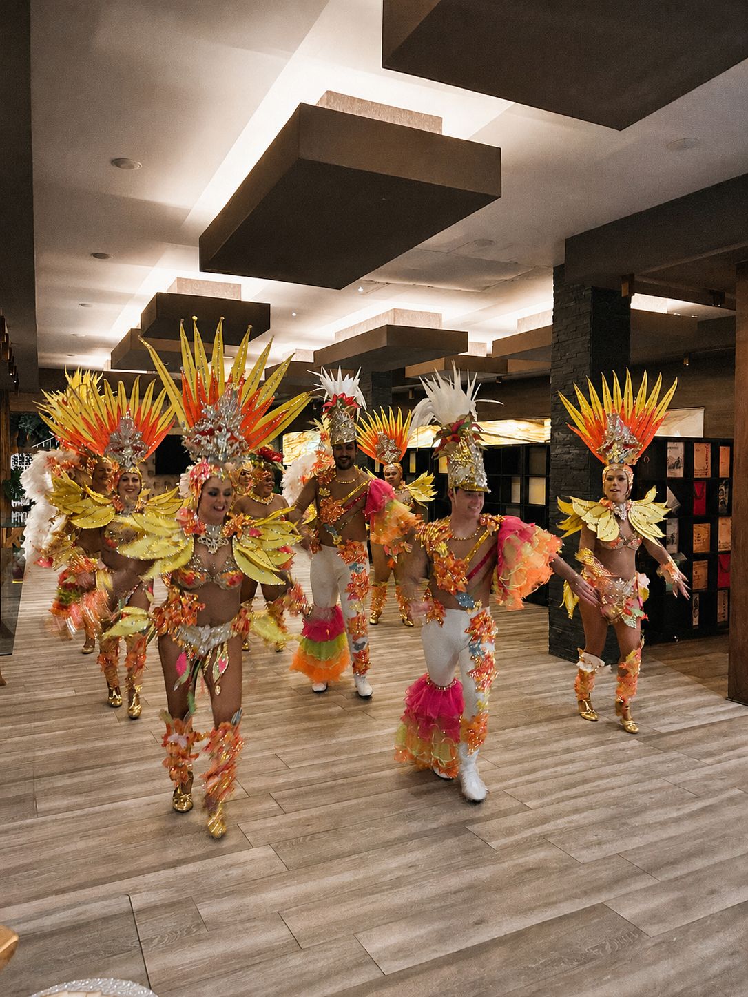 Un grupo de bailarines con trajes de plumas y lentejuelas actúa para los invitados en el interior del local